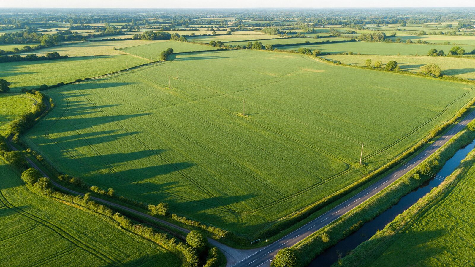 Aerial view of large flat undeveloped farmland parcels bordered by a road and a creek.